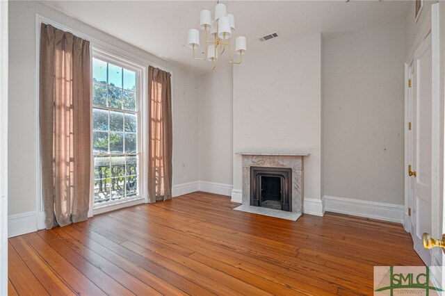 unfurnished living room with hardwood / wood-style floors, a high end fireplace, and a chandelier