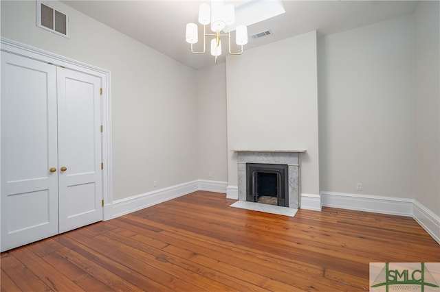 unfurnished living room with wood-type flooring, a fireplace, and an inviting chandelier