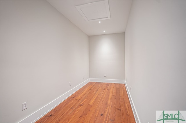 unfurnished room with attic access, light wood-type flooring, and baseboards