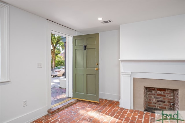 entryway with visible vents, a fireplace with flush hearth, recessed lighting, brick floor, and baseboards