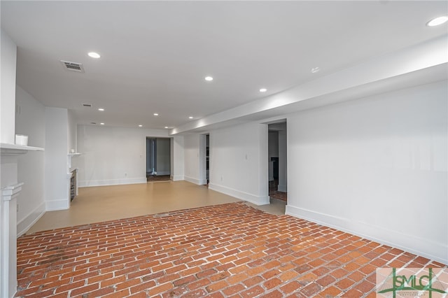 below grade area with visible vents, recessed lighting, baseboards, and brick floor