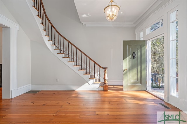 entryway with light wood-type flooring, crown molding, and an inviting chandelier