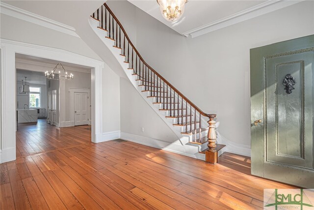 foyer entrance with hardwood / wood-style flooring, ornamental molding, and a chandelier