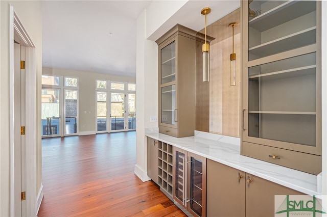 bar featuring light stone counters, pendant lighting, beverage cooler, and wood-type flooring