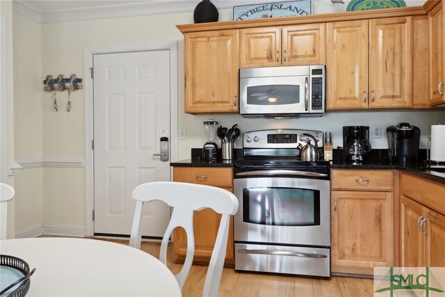 kitchen featuring dark stone counters, ornamental molding, stainless steel appliances, and light wood-type flooring