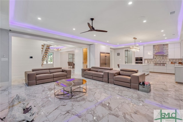 tiled living room with ceiling fan with notable chandelier and a raised ceiling