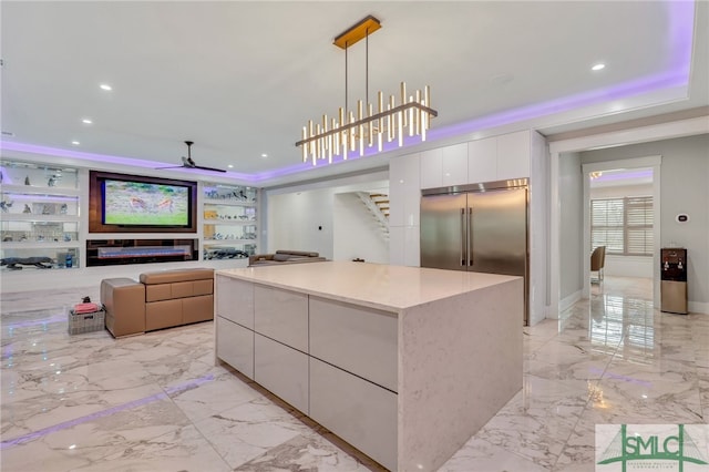 kitchen with built in fridge, white cabinets, a kitchen island, ceiling fan with notable chandelier, and hanging light fixtures