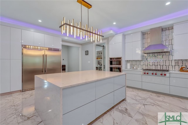 kitchen featuring pendant lighting, stainless steel appliances, a kitchen island, wall chimney range hood, and white cabinetry