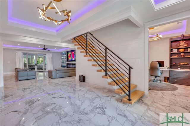 staircase featuring a raised ceiling, light tile flooring, and ceiling fan with notable chandelier