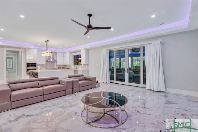 tiled living room with ceiling fan with notable chandelier, a wealth of natural light, and a tray ceiling