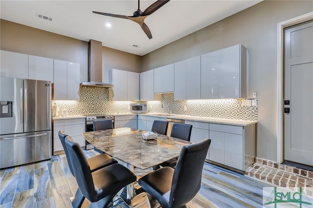 kitchen featuring white cabinetry, backsplash, ceiling fan, stainless steel fridge with ice dispenser, and wall chimney exhaust hood