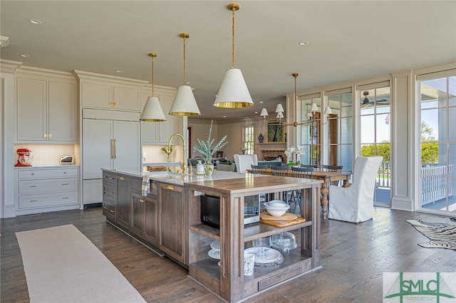 kitchen featuring pendant lighting, paneled built in fridge, a brick fireplace, a kitchen island with sink, and dark hardwood / wood-style floors