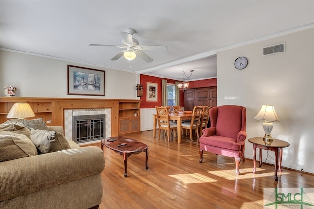 116 E 66th St, Savannah, GA 31405 - living room featuring light hardwood / wood-style flooring, a tiled fireplace, ornamental molding, and ceiling fan with notable chandelier