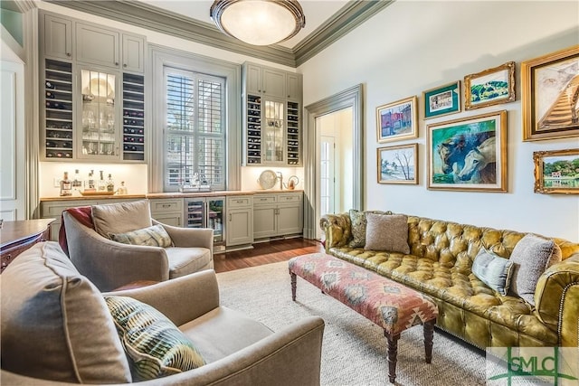 sitting room with dark wood-type flooring, beverage cooler, bar, and crown molding
