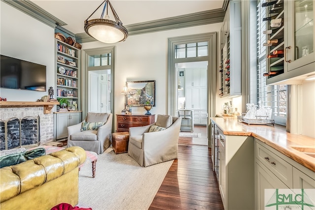 living room with built in shelves, dark hardwood / wood-style flooring, a fireplace, and crown molding