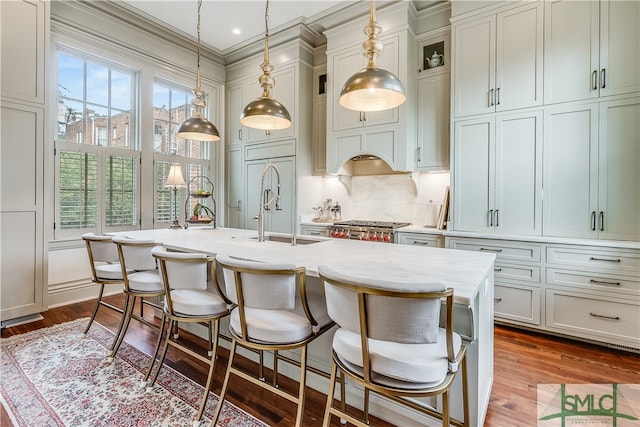 kitchen with decorative light fixtures, backsplash, hardwood / wood-style floors, an island with sink, and sink