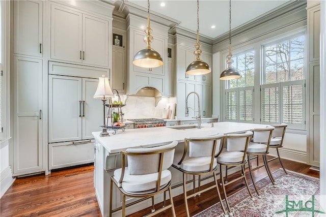 kitchen with crown molding, a sink, light countertops, wood finished floors, and an island with sink