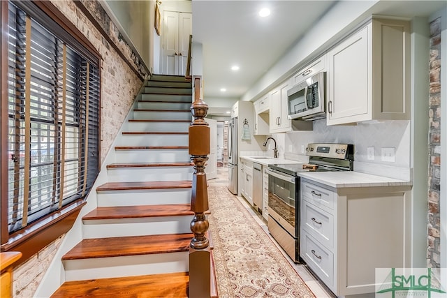 kitchen featuring backsplash, white cabinetry, light wood-type flooring, appliances with stainless steel finishes, and sink