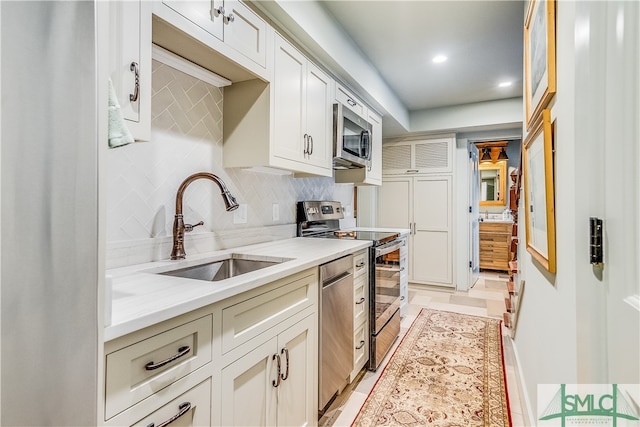 kitchen with stainless steel appliances, light tile flooring, backsplash, sink, and white cabinets