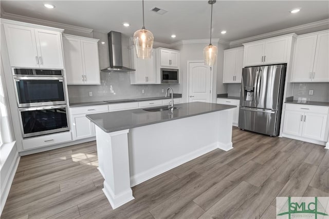 kitchen featuring stainless steel appliances, dark countertops, hanging light fixtures, a sink, and wall chimney exhaust hood