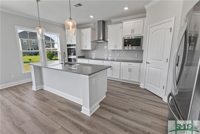 kitchen with hanging light fixtures, wall chimney range hood, appliances with stainless steel finishes, and white cabinetry