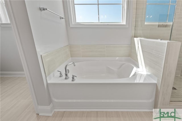 full bath with tiled shower, a garden tub, and baseboards