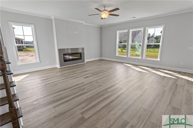 unfurnished living room featuring light wood-type flooring, a healthy amount of sunlight, ornamental molding, and a glass covered fireplace