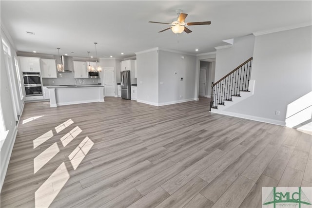 unfurnished living room featuring light wood-type flooring, stairway, baseboards, and ceiling fan with notable chandelier