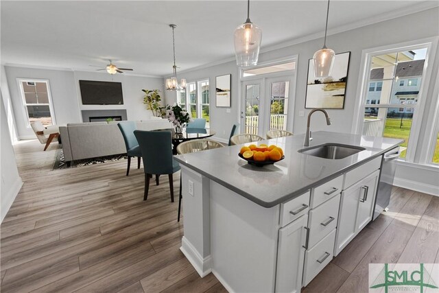 kitchen featuring decorative light fixtures, a sink, white cabinetry, dishwasher, and a center island with sink