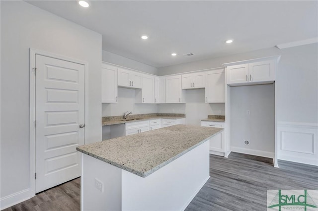 kitchen with dark wood-type flooring, sink, a center island, light stone countertops, and white cabinets