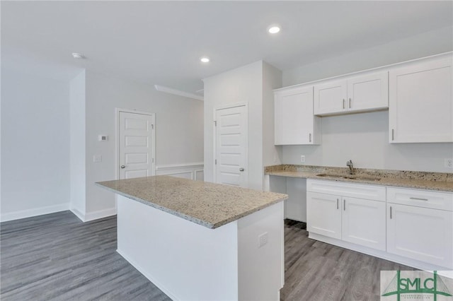 kitchen featuring a kitchen island, white cabinetry, sink, hardwood / wood-style flooring, and light stone countertops