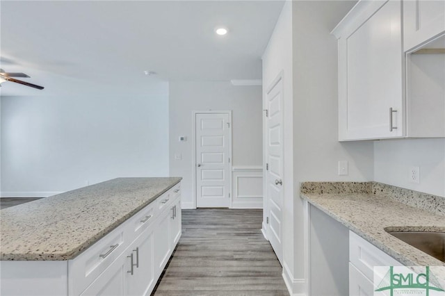 kitchen with light stone counters, ceiling fan, wood-type flooring, and white cabinets