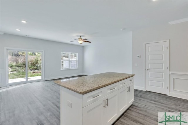 kitchen with white cabinetry, a kitchen island, ceiling fan, light stone countertops, and hardwood / wood-style floors