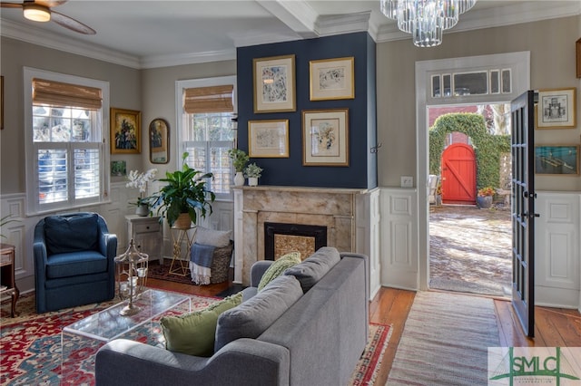 living room with light hardwood / wood-style flooring, ornamental molding, a high end fireplace, and ceiling fan with notable chandelier