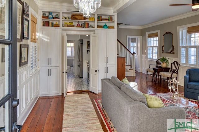 living room with ornamental molding, dark wood-type flooring, and ceiling fan with notable chandelier