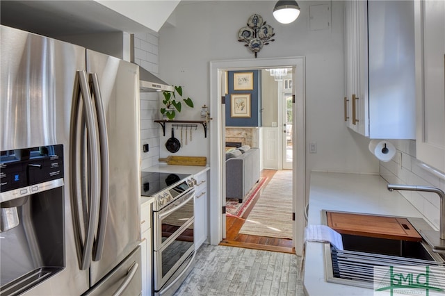 kitchen featuring white cabinetry, appliances with stainless steel finishes, light hardwood / wood-style flooring, ventilation hood, and tasteful backsplash