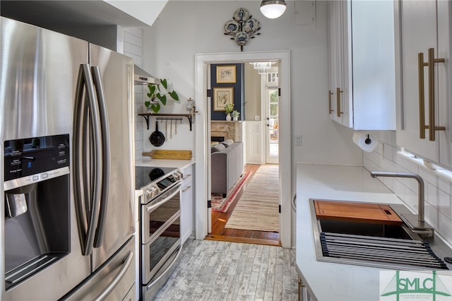 kitchen featuring appliances with stainless steel finishes, white cabinetry, light wood-type flooring, backsplash, and sink