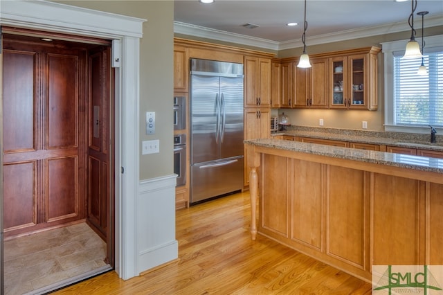 kitchen with appliances with stainless steel finishes, hanging light fixtures, light wood-type flooring, and light stone counters