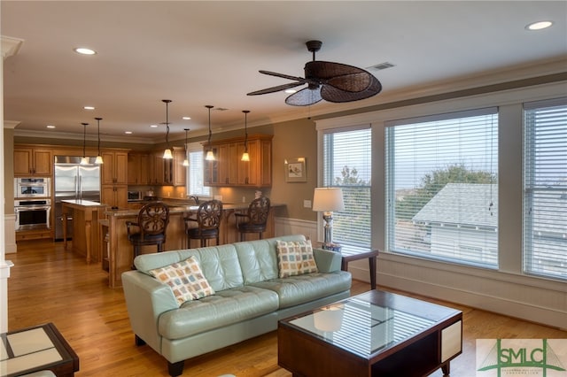 living room featuring ceiling fan, crown molding, light wood-type flooring, and plenty of natural light