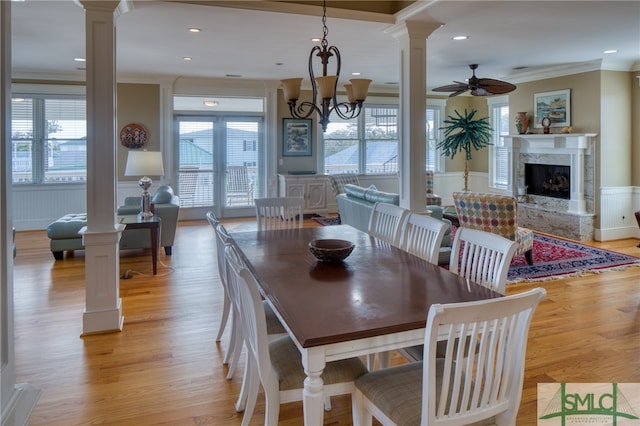 dining room with light hardwood / wood-style floors, a fireplace, ceiling fan with notable chandelier, crown molding, and ornate columns