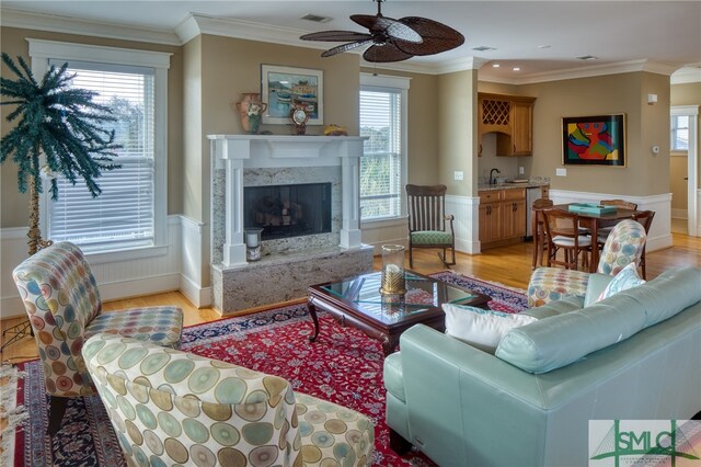 living room with ornamental molding, a premium fireplace, a wealth of natural light, and light hardwood / wood-style flooring