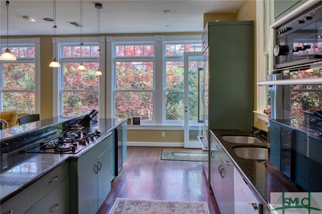 kitchen featuring dark stone countertops, hanging light fixtures, dark hardwood / wood-style flooring, and a healthy amount of sunlight