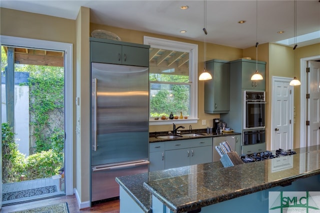 kitchen featuring pendant lighting, dark stone countertops, appliances with stainless steel finishes, and sink