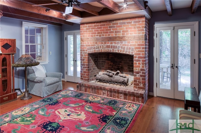 living room with french doors, a brick fireplace, ceiling fan, hardwood / wood-style floors, and beam ceiling