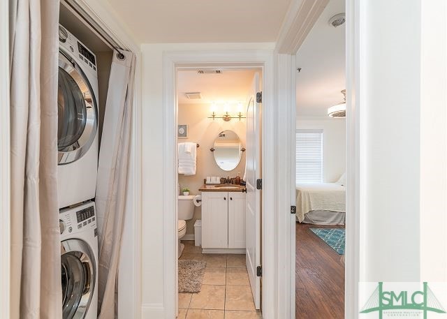 laundry room with light tile patterned floors, stacked washer and clothes dryer, a sink, and laundry area