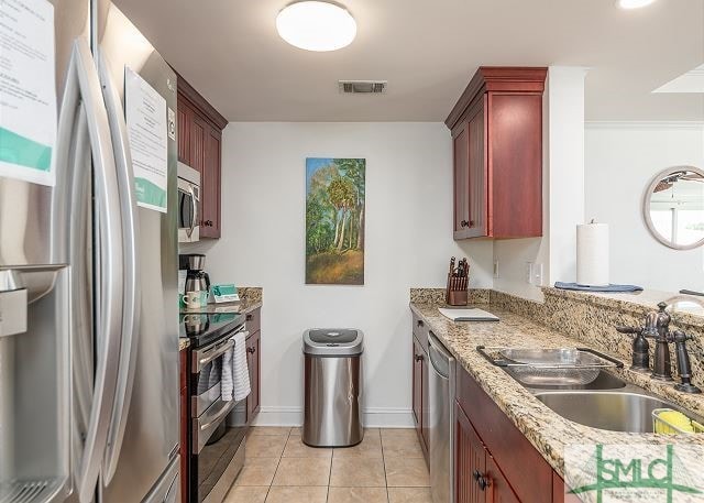 kitchen featuring light tile patterned flooring, visible vents, appliances with stainless steel finishes, reddish brown cabinets, and a sink