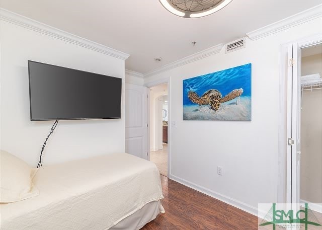bedroom with baseboards, ornamental molding, visible vents, and wood finished floors