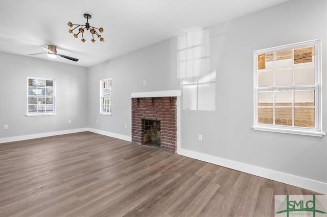 unfurnished living room featuring hardwood / wood-style floors, ceiling fan with notable chandelier, and a brick fireplace