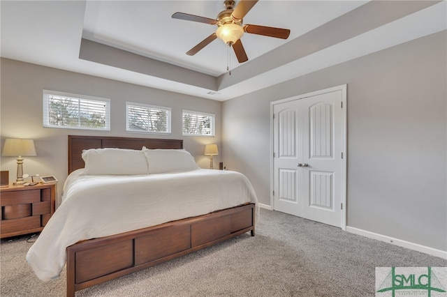 carpeted bedroom with a raised ceiling, a closet, and ceiling fan