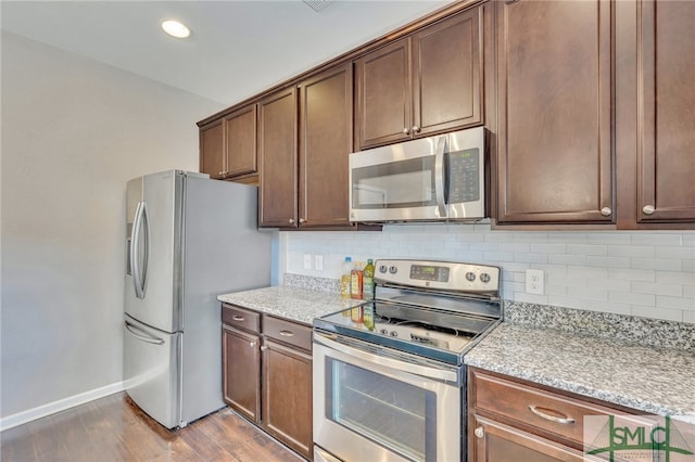 kitchen with appliances with stainless steel finishes, light stone counters, tasteful backsplash, dark brown cabinets, and light hardwood / wood-style flooring